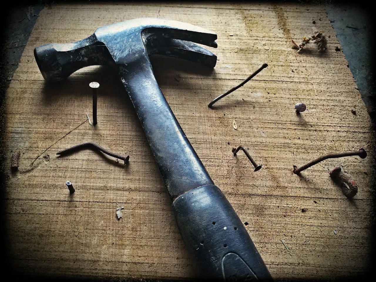 services-03 A weathered hammer surrounded by bent nails on a wooden plank, capturing the essence of carpentry work.
