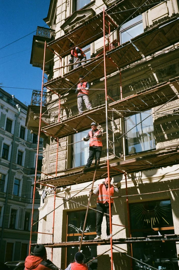 our-story Construction workers on scaffolding renovating a building facade on a sunny day.