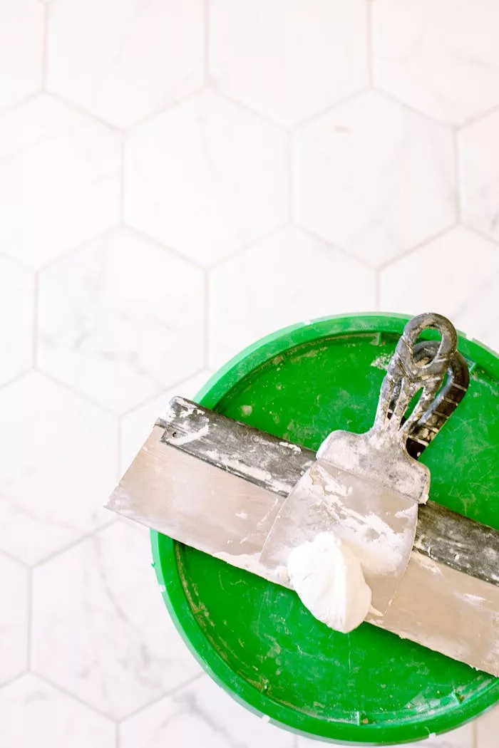services-04 Close-up of a trowel and putty on a green bucket, ideal for renovation projects.