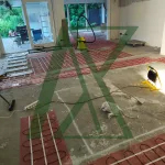 Installation von elektrischen Fußbodenheizmatten in einem offenen Wohnbereich während der Sanierung; sichtbare Heizmatten, vorbereiteter Estrichboden und Baustellenwerkzeuge.