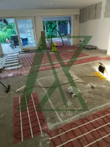 Installation von elektrischen Fußbodenheizmatten in einem offenen Wohnbereich während der Sanierung; sichtbare Heizmatten, vorbereiteter Estrichboden und Baustellenwerkzeuge.