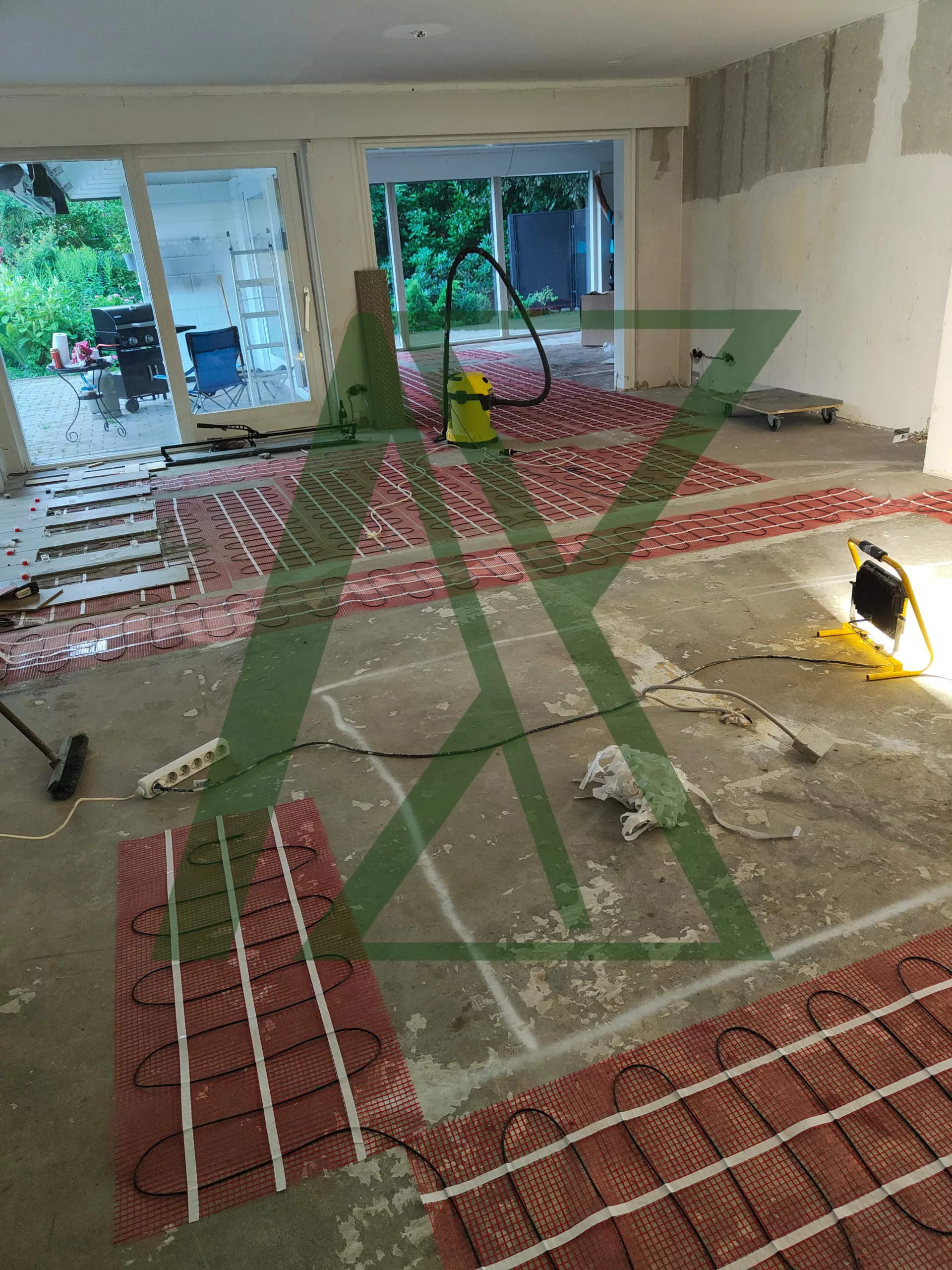 Installation von elektrischen Fußbodenheizmatten in einem offenen Wohnbereich während der Sanierung; sichtbare Heizmatten, vorbereiteter Estrichboden und Baustellenwerkzeuge.