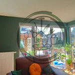 Renovierter Wohn- und Essbereich mit großen Fensterfronten, frisch gestrichenen Wänden in Grün und Weiß, Pflanzen und moderner Einrichtung.