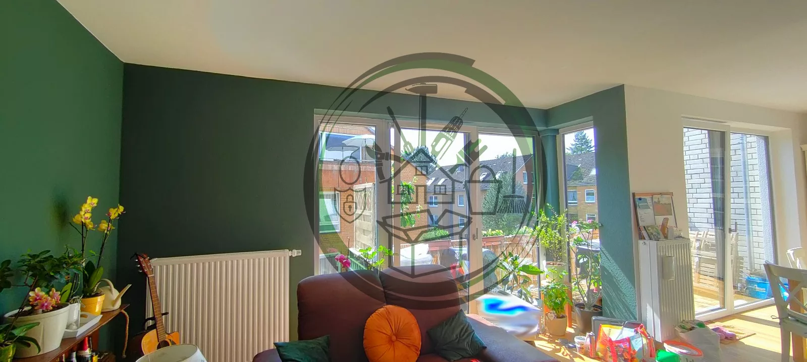 Renovierter Wohn- und Essbereich mit großen Fensterfronten, frisch gestrichenen Wänden in Grün und Weiß, Pflanzen und moderner Einrichtung.